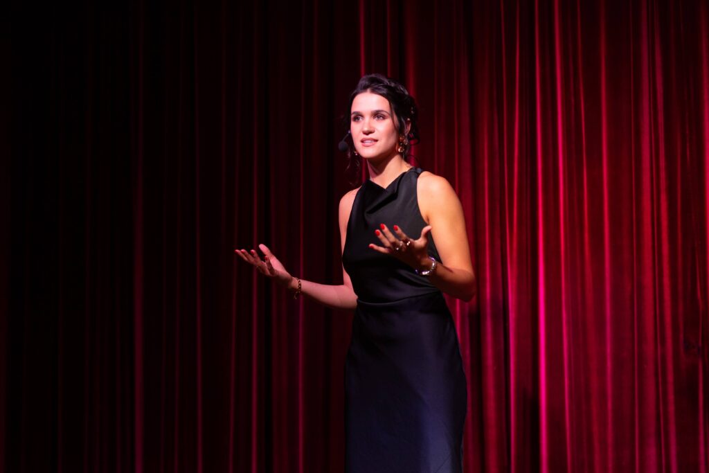 Julia Guz wearing a dark dress onstage presenting in front of a red curtain