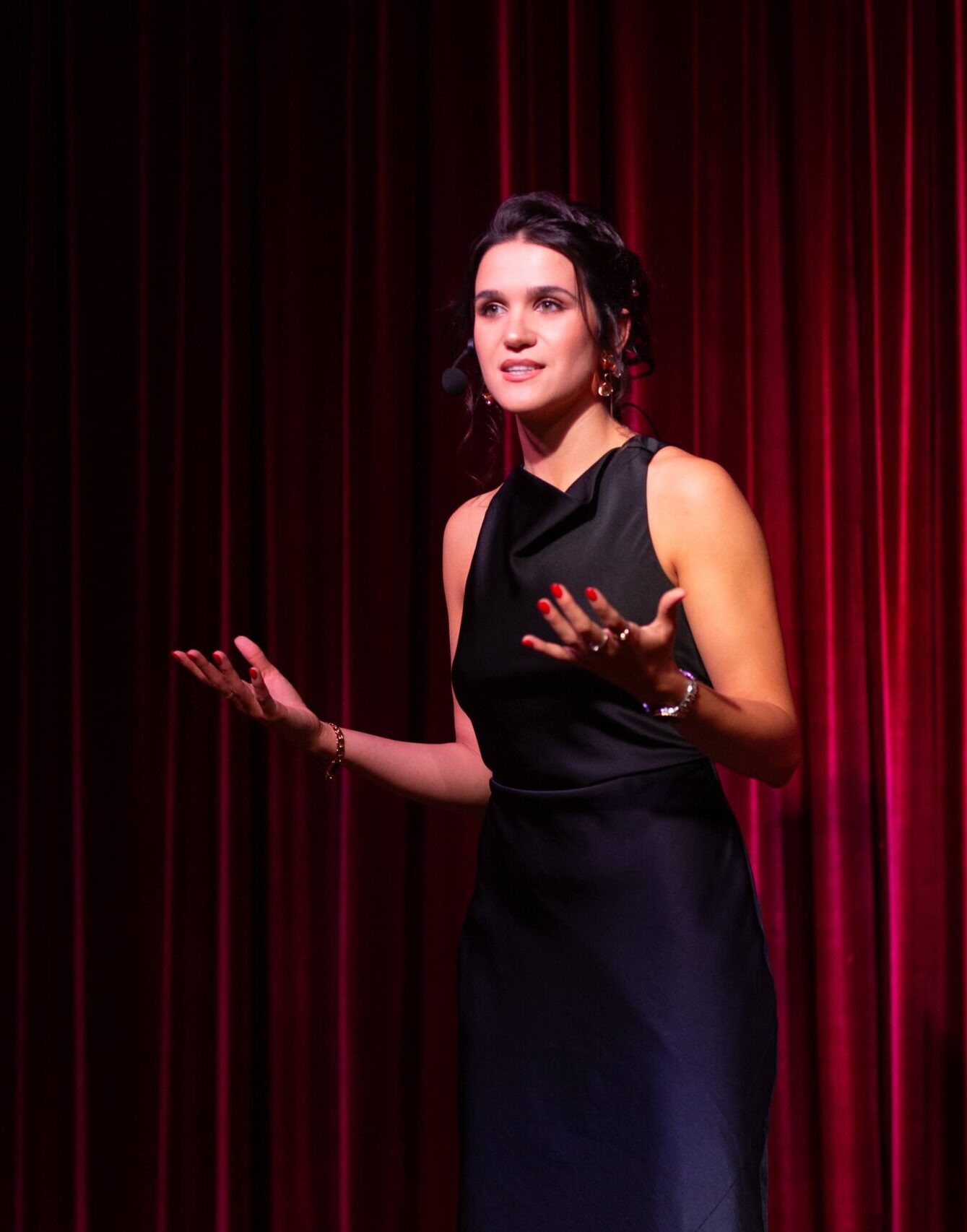 Julia Guz wearing a dark dress onstage presenting in front of a red curtain