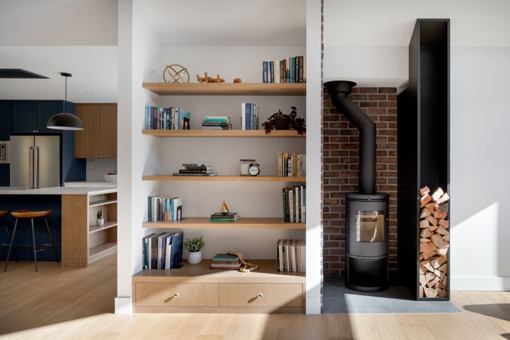 “A stylish built-in bookshelf and fireplace designed by Cara Hansen of Triple Dot Design Studio. The bookshelf features neatly arranged books, decorative objects, and greenery, seamlessly blending function and style. The modern fireplace, framed by clean lines and natural textures, adds warmth and sophistication to the space, showcasing Cara’s timeless design approach