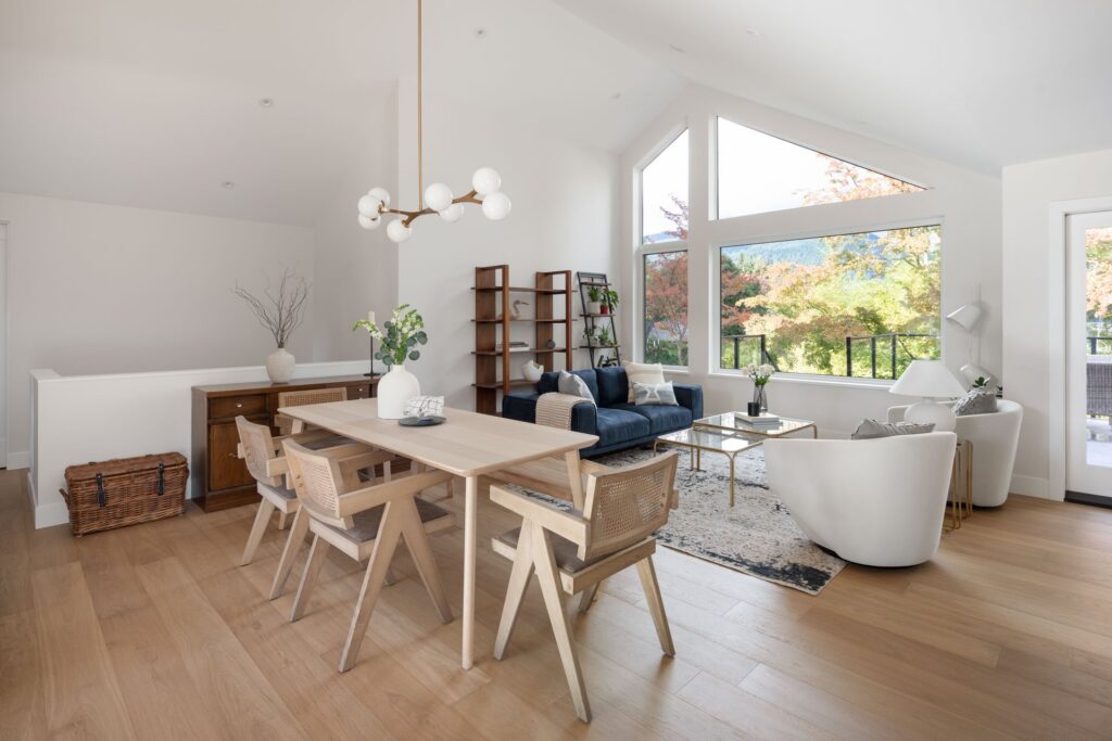 A beautifully designed living room by Cara Hansen of Triple Dot Design Studio, featuring a warm neutral colour palette, a plush sectional sofa, a sleek wooden coffee table, and soft-textured area rugs. The space is accented with greenery, modern lighting, and clean-lined decor, embodying a balance of Scandinavian simplicity and West Coast charm