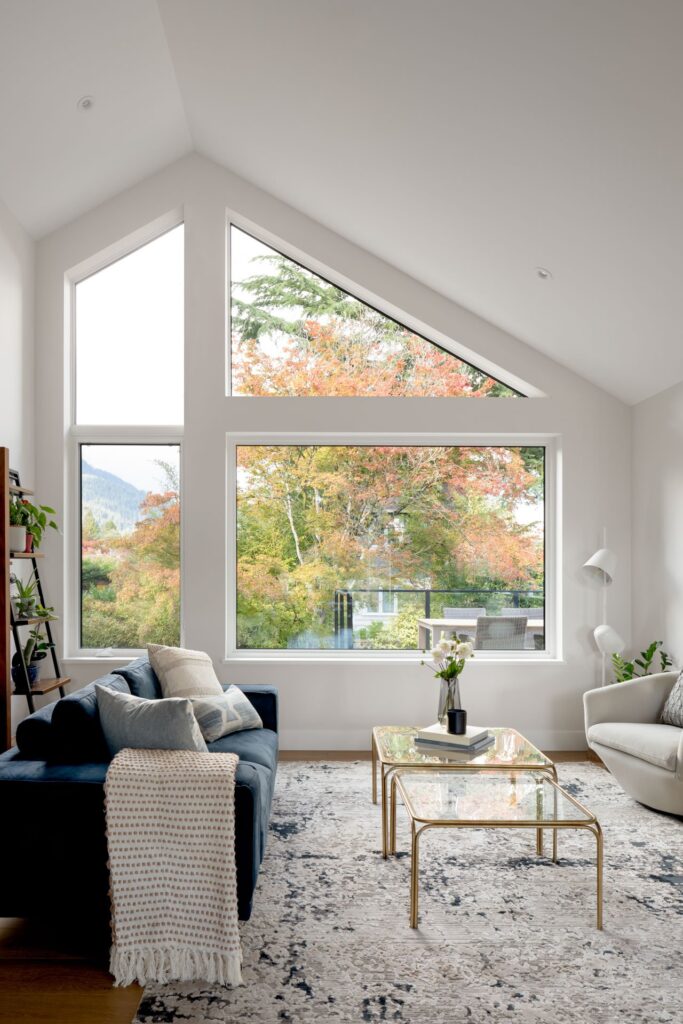 A beautifully designed living room by Cara Hansen of Triple Dot Design Studio, featuring a warm neutral colour palette, a plush sectional sofa, a sleek wooden coffee table, and soft-textured area rugs. The space is accented with greenery, modern lighting, and clean-lined decor, embodying a balance of Scandinavian simplicity and West Coast charm