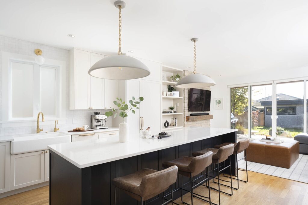 A modern kitchen designed by Cara Hansen of Triple Dot Design Studio, featuring sleek cabinetry in a neutral tone, a spacious island with bar seating, and elegant pendant lighting. The design incorporates clean lines, high-end finishes, and functional layouts, blending Scandinavian practicality with West Coast-inspired warmth