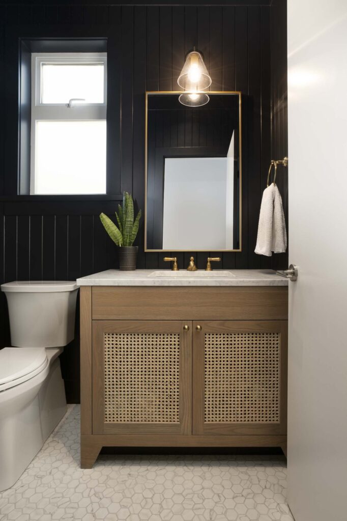 A luxurious dark bathroom designed by Cara Hansen of Triple Dot Design Studio, featuring rich, moody tones, sleek black fixtures, and a freestanding soaking tub. Subtle lighting highlights the elegant tilework and creates a spa-like ambiance, blending sophistication with modern design